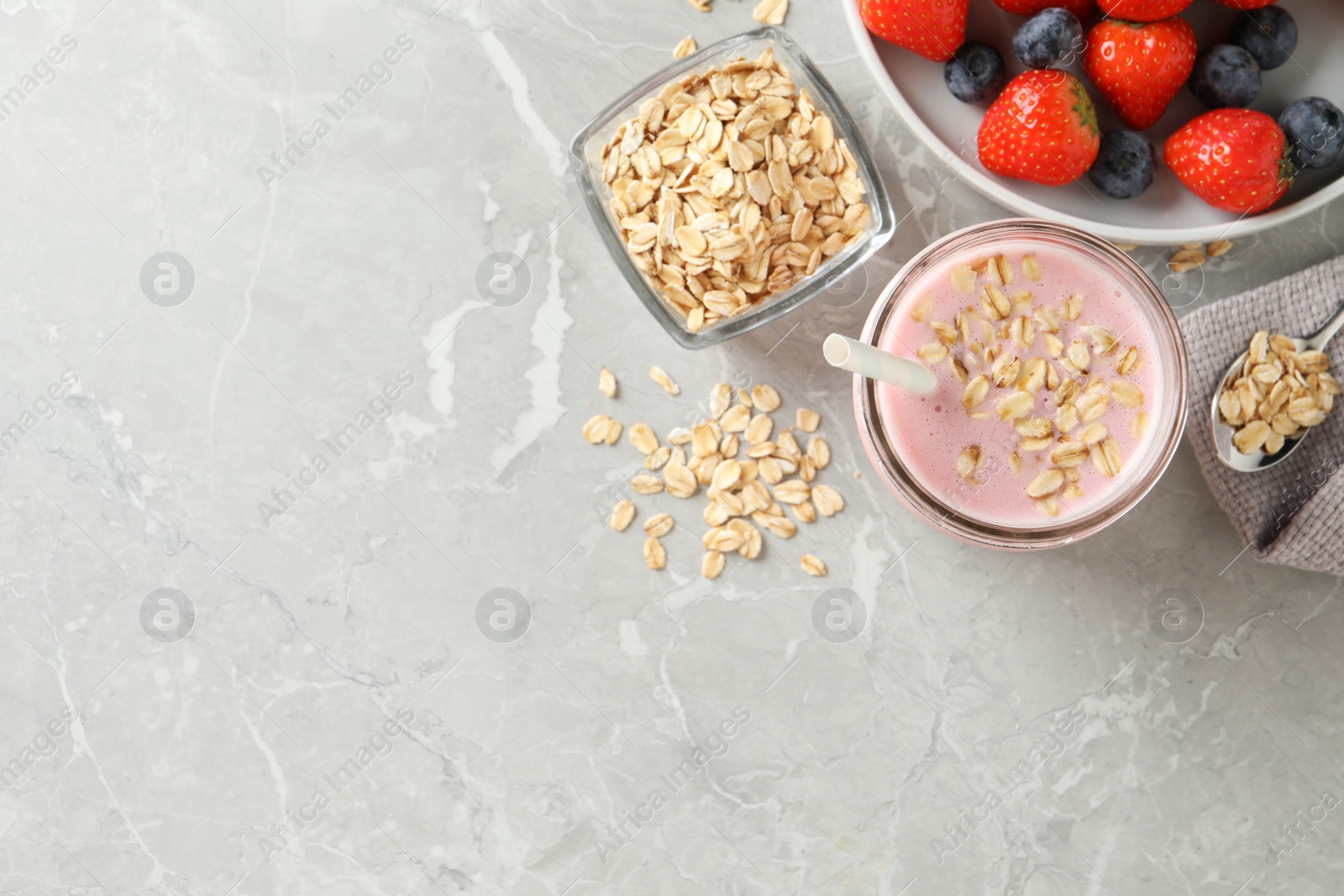 Photo of Jar of tasty berry oatmeal smoothie and ingredients on grey table, flat lay. Space for text