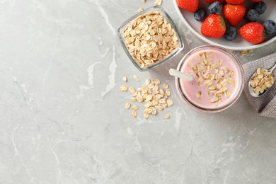 Photo of Jar of tasty berry oatmeal smoothie and ingredients on grey table, flat lay. Space for text
