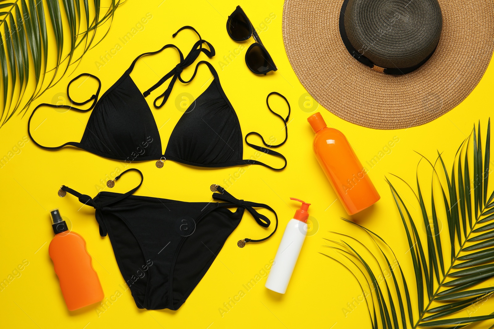 Photo of Flat lay composition with black swimsuit and beach accessories on yellow background