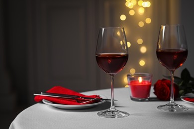 Photo of Romantic table setting with glasses of red wine, rose flower and burning candle against blurred lights, space for text