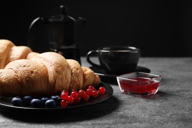 Plate with fresh crispy croissant and berries on grey table. Space for text