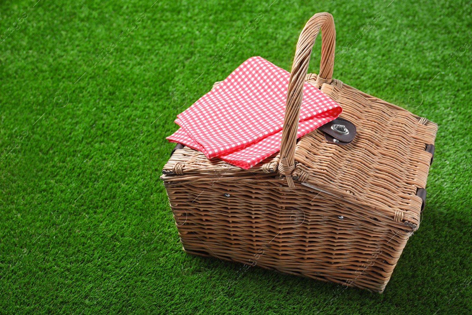 Photo of Checkered tablecloth and closed wicker picnic basket on green grass, space for text