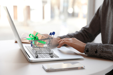 Image of Woman shopping online using laptop, small cart with box on computer