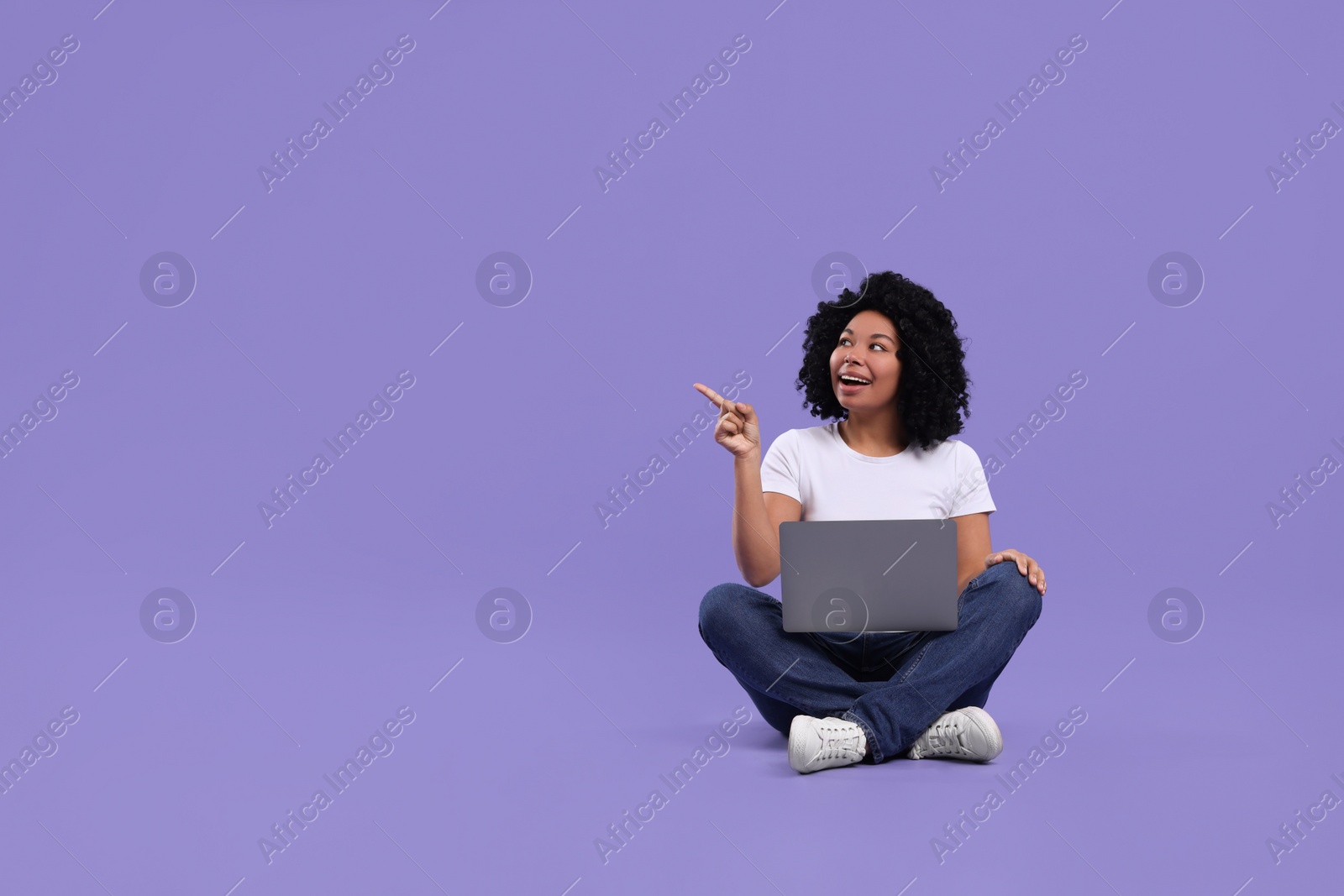 Photo of Happy young woman with laptop pointing at something on purple background. Space for text