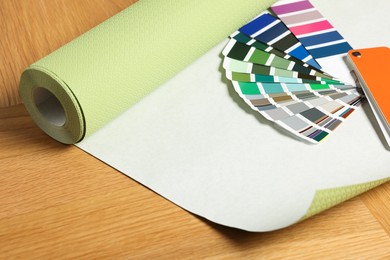 Photo of Green wallpaper roll and color palette samples on wooden table