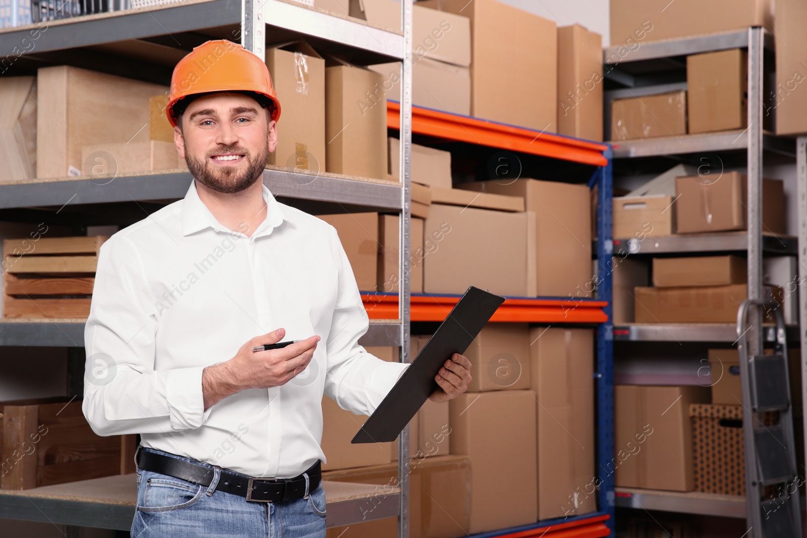 Photo of Young man with clipboard near rack of cardboard boxes at warehouse