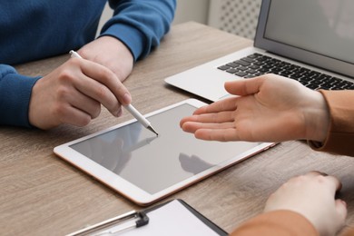 Photo of Businesspeople using modern tablet at wooden desk indoors, closeup