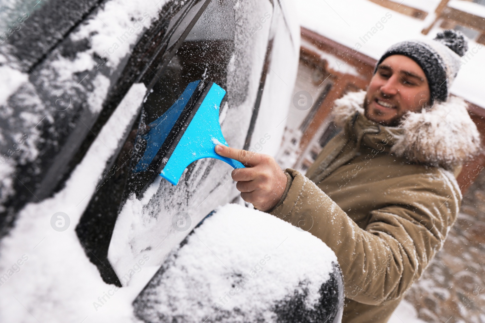 Photo of Young man cleaning snow from car window outdoors on winter day