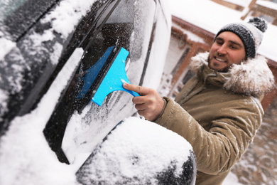 Photo of Young man cleaning snow from car window outdoors on winter day