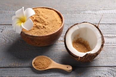 Coconut sugar, bowl, spoon, flower and fruit on grey wooden table, closeup