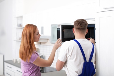 Housewife and repairman near microwave oven in kitchen