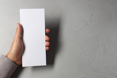 Man holding white blank card at light grey table, top view. Mockup for design