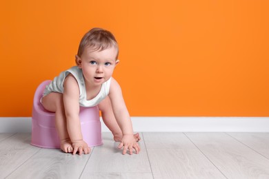 Photo of Little child sitting on baby potty near orange wall. Space for text