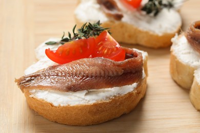 Delicious sandwiches with cream cheese, anchovy and tomatoes on wooden board, closeup