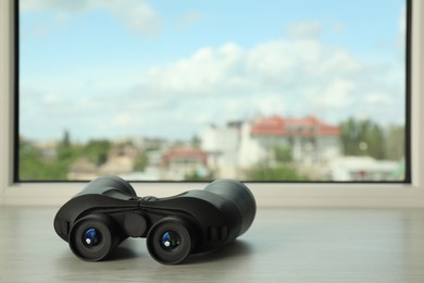 Photo of Black binoculars on white wooden window sill. Space for text