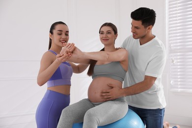 Pregnant woman and her husband working with trainer in gym. Preparation for child birth