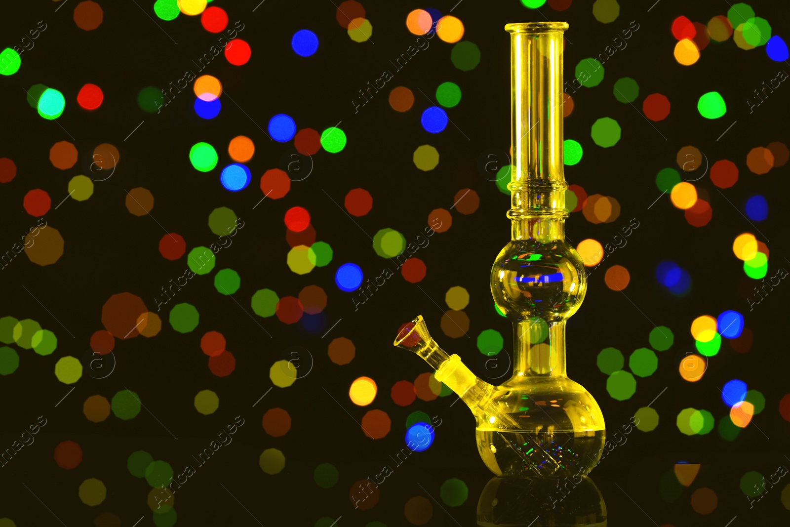 Photo of Glass bong against blurred lights, space for text. Smoking device