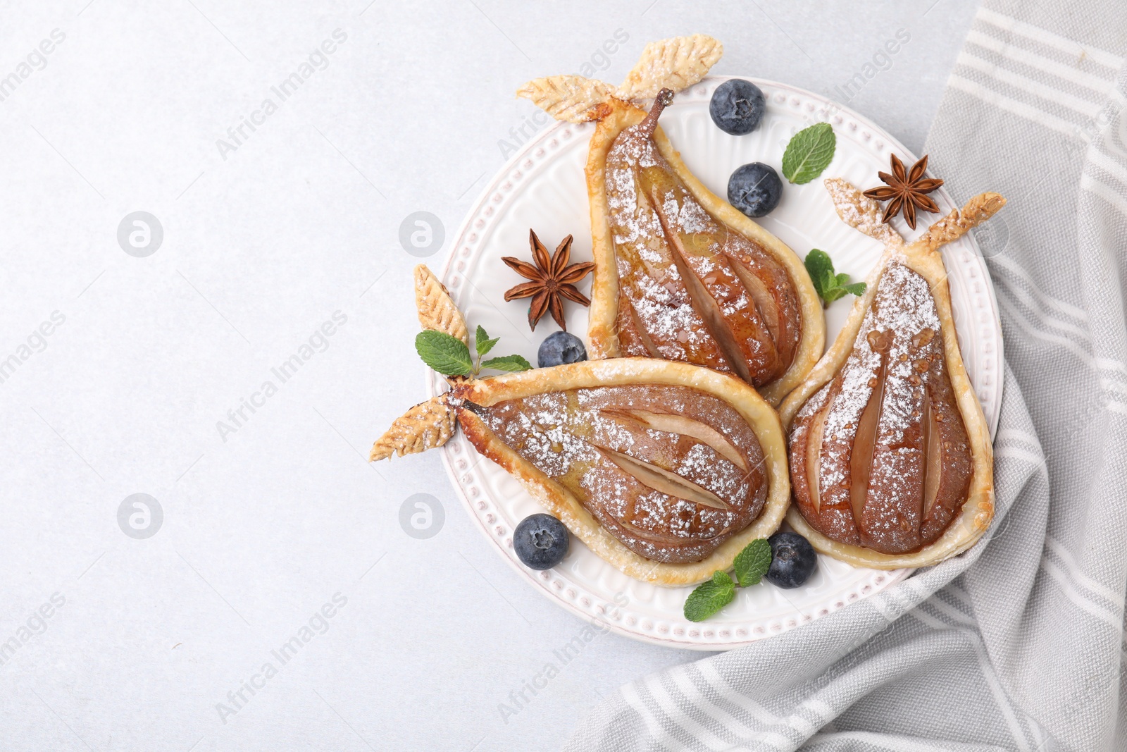 Photo of Delicious pears baked in puff pastry with powdered sugar on light table, top view. Space for text