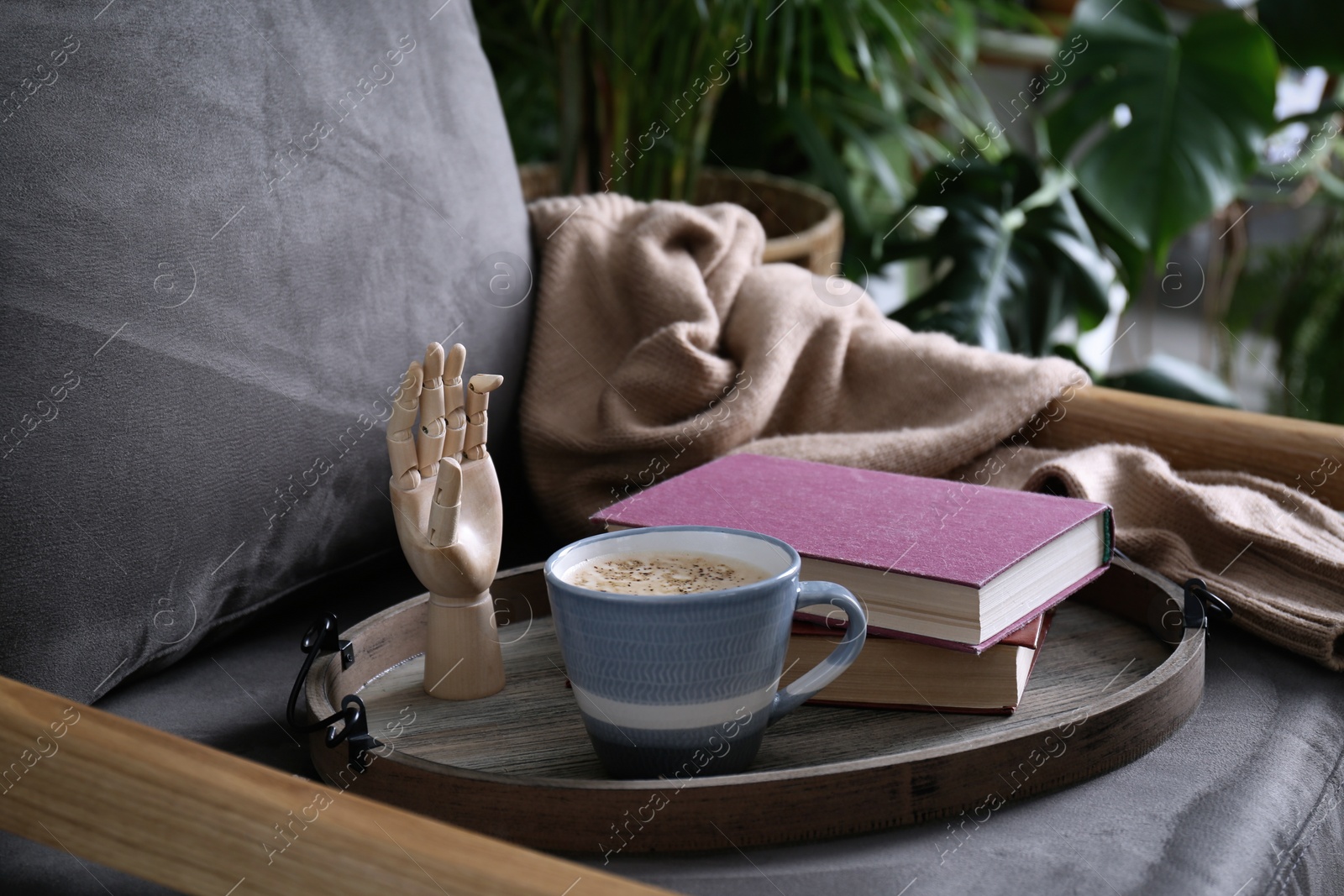 Photo of Wooden tray with books and coffee on armchair indoors