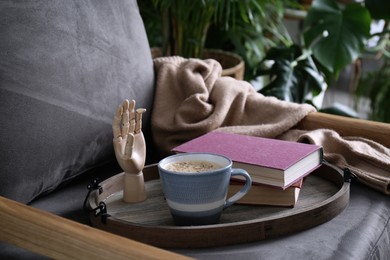 Wooden tray with books and coffee on armchair indoors