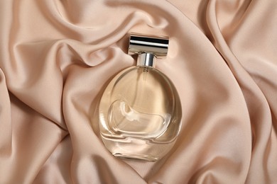 Luxury perfume in bottle on beige silk fabric, top view