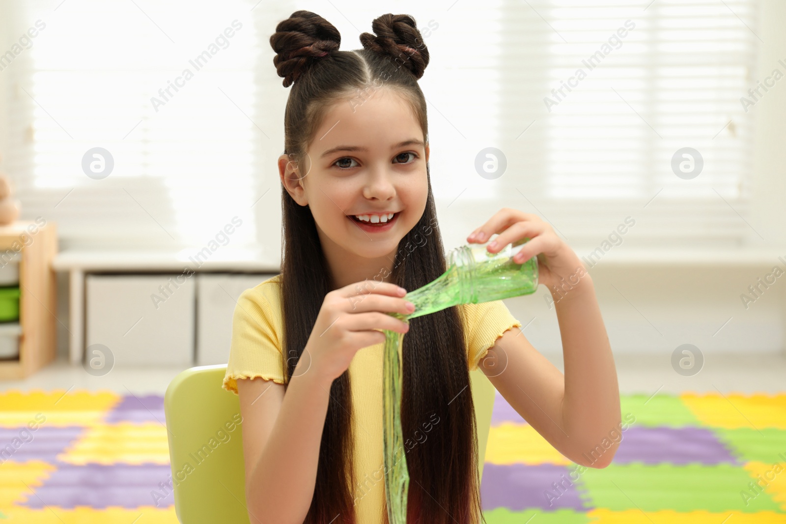 Photo of Little girl playing with slime in room