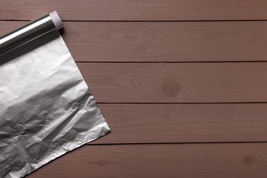 Roll of aluminum foil on wooden table, top view. Space for text