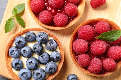 Tartlets with different fresh berries on wooden board, flat lay. Delicious dessert