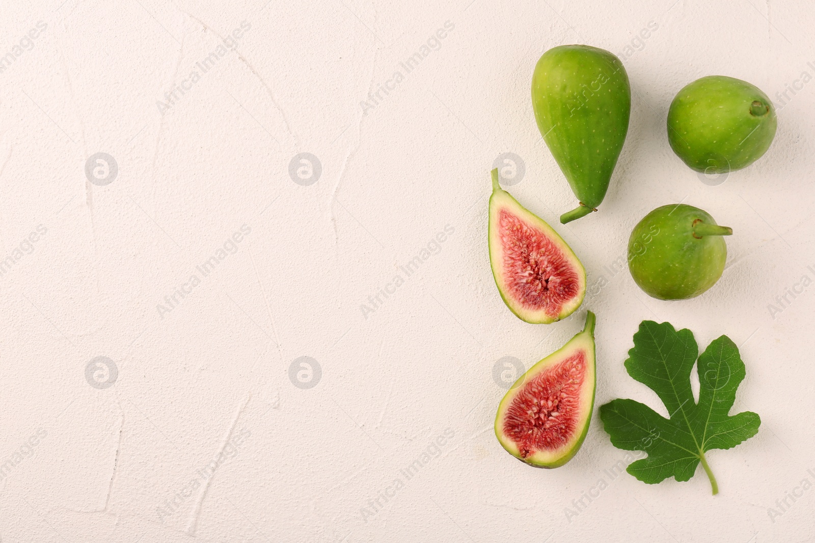 Photo of Cut and whole green figs with leaf on light table, flat lay. Space for text
