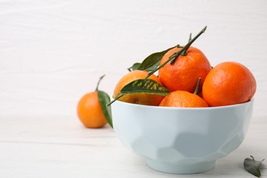 Photo of Bowl with fresh ripe tangerines and leaves on white table, space for text