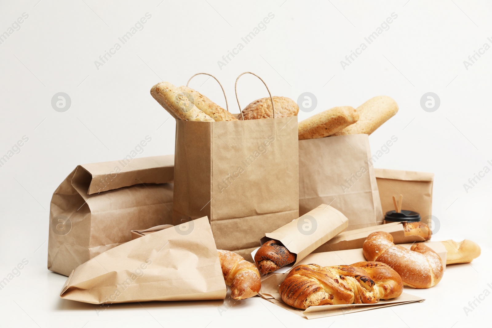 Photo of Different fresh bakery products in paper bags on white background