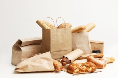 Different fresh bakery products in paper bags on white background