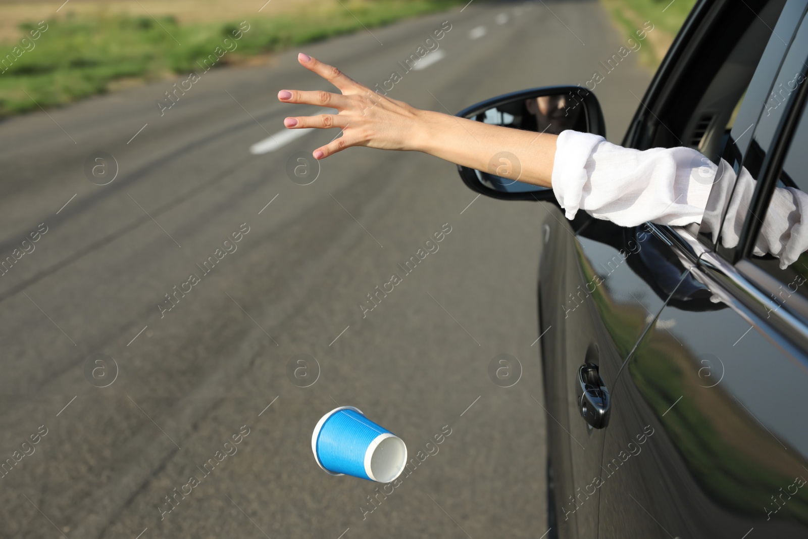 Photo of Driver throwing away paper cup from car window. Garbage on road