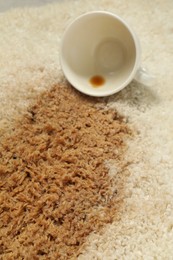 Photo of Overturned cup and spilled coffee on beige carpet, closeup