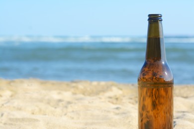 Photo of Bottle of beer on beach near sea, closeup. Space for text