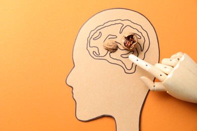 Photo of Amnesia problem. Paper cutout of human head, brain drawing, broken walnut and mannequin hand on orange background, top view