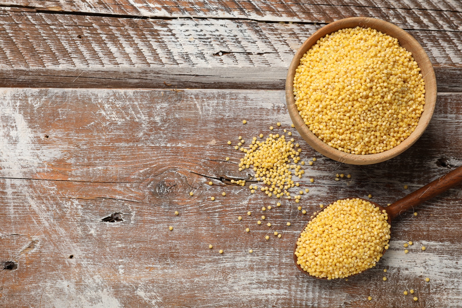 Photo of Millet groats in bowl and spoon on wooden table, flat lay. Space for text