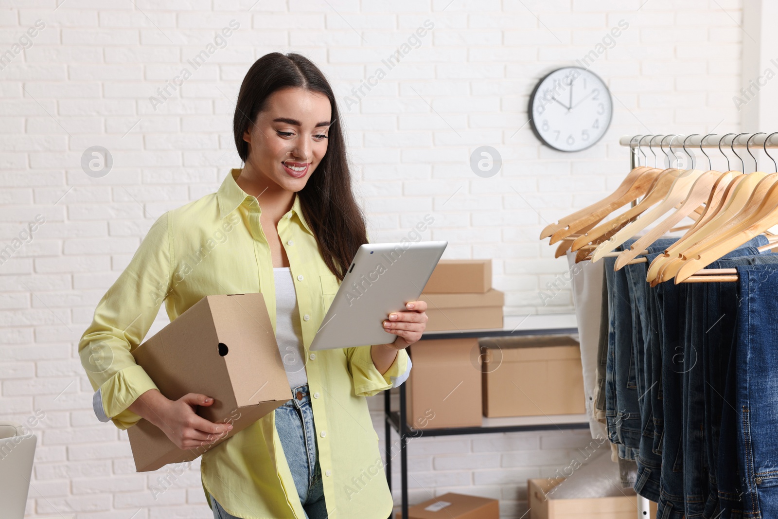 Photo of Clothes seller with parcel and tablet in office. Online store