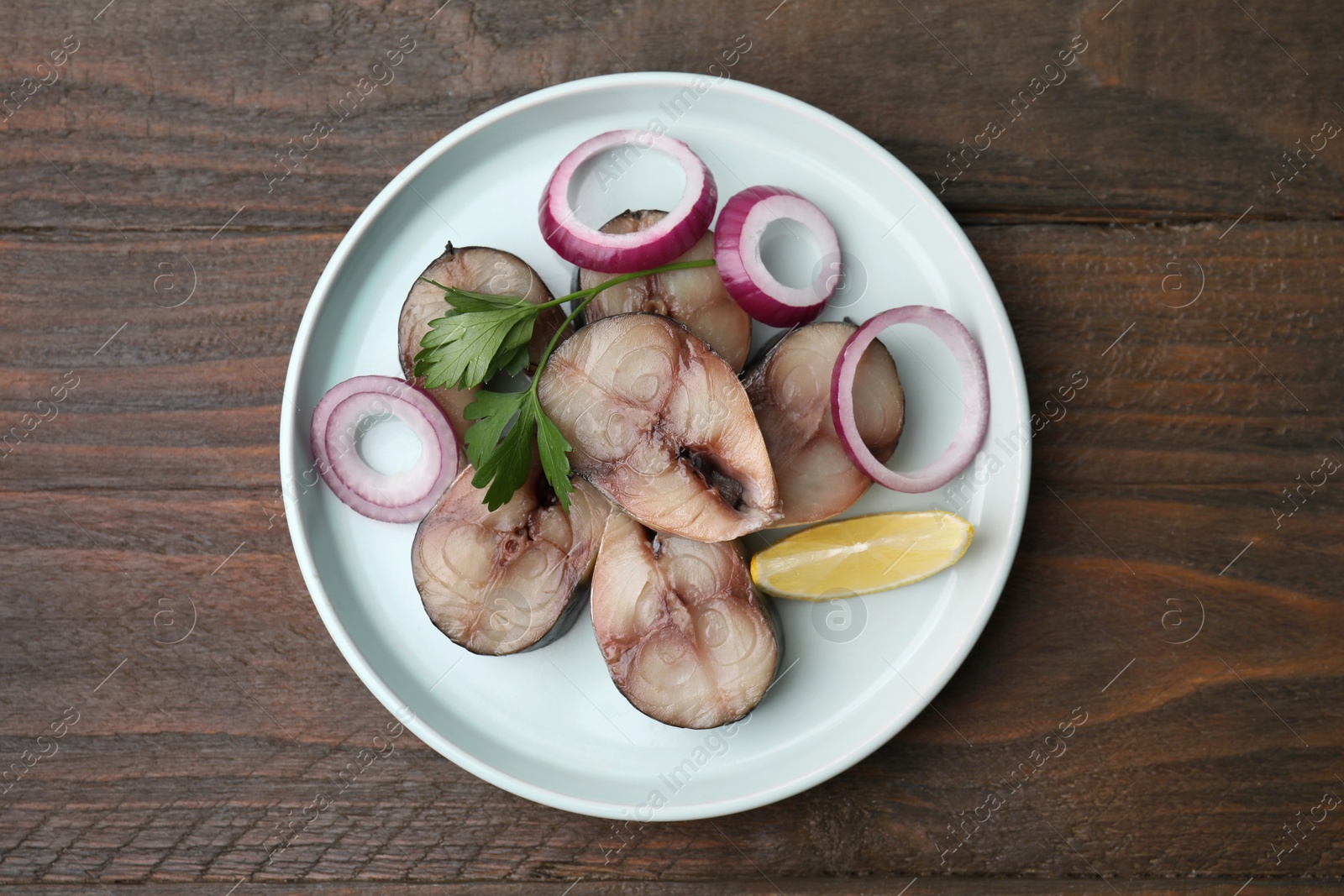 Photo of Slices of tasty salted mackerel with onion rings, parsley and lemon wedge on wooden table, top view