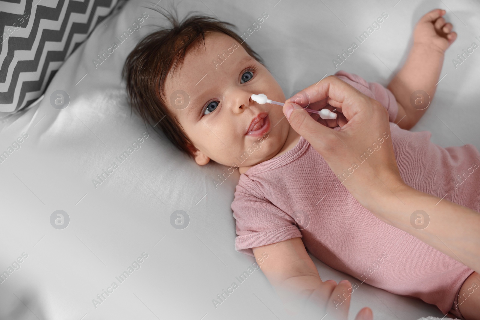 Photo of Mother cleaning nose of her baby with cotton bud on bed, closeup