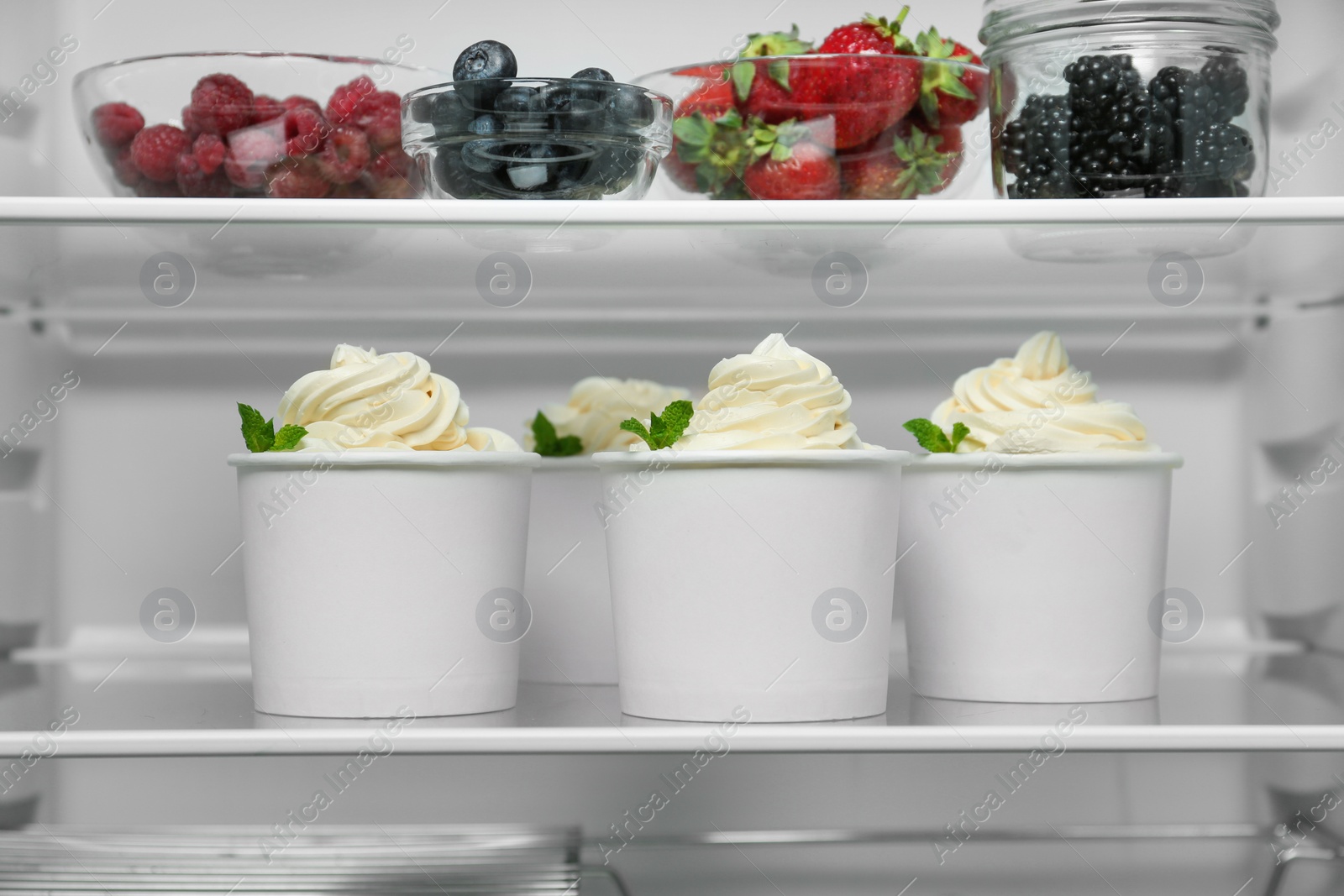 Photo of Cups with tasty frozen yogurt on fridge shelf