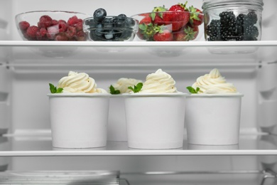 Cups with tasty frozen yogurt on fridge shelf