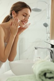 Photo of Young woman applying cleansing foam onto her face in bathroom