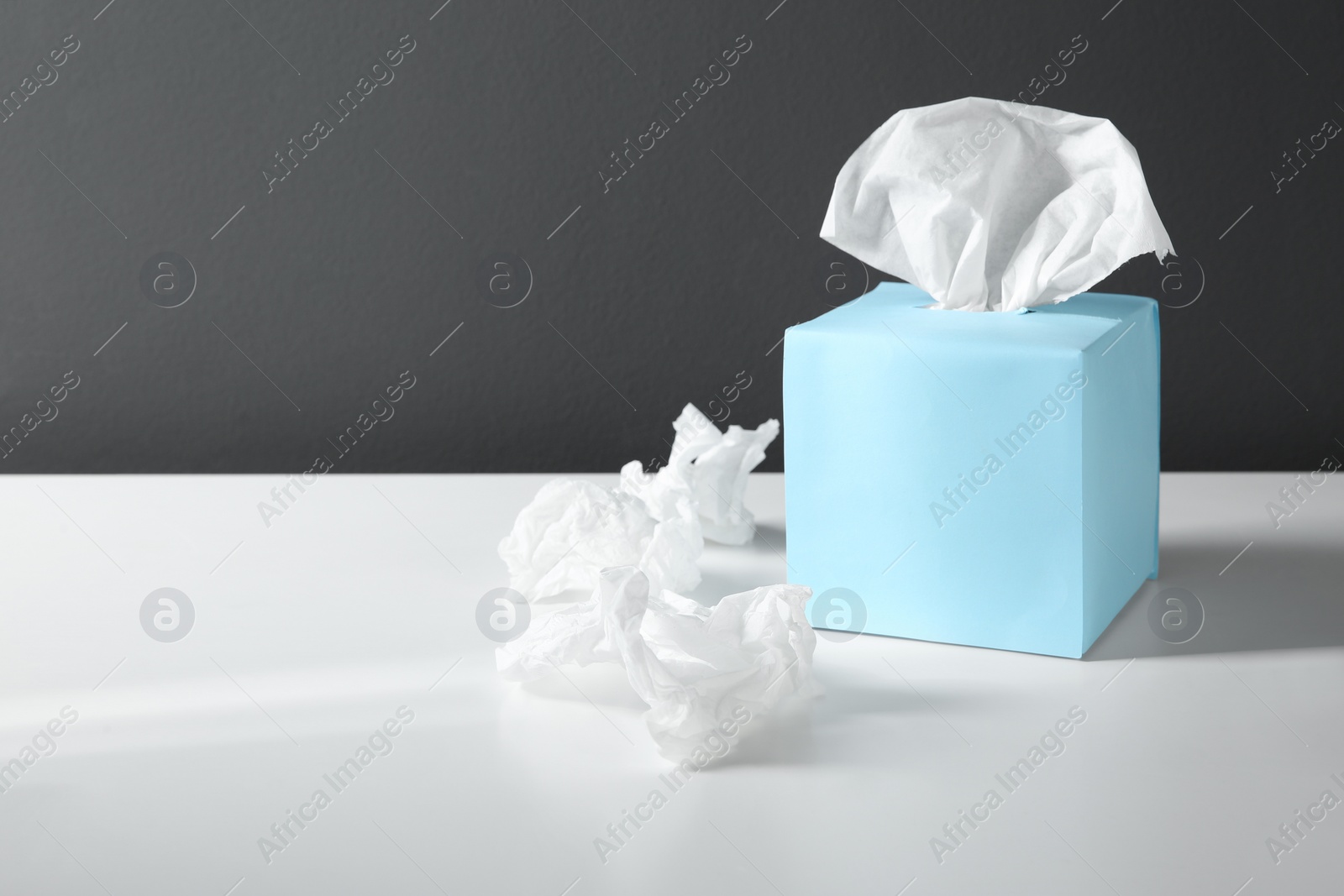 Photo of Used paper tissues and blue box on white table. Space for text