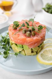 Tasty salmon tartare with avocado, lemon, capers and microgreens on white table, closeup