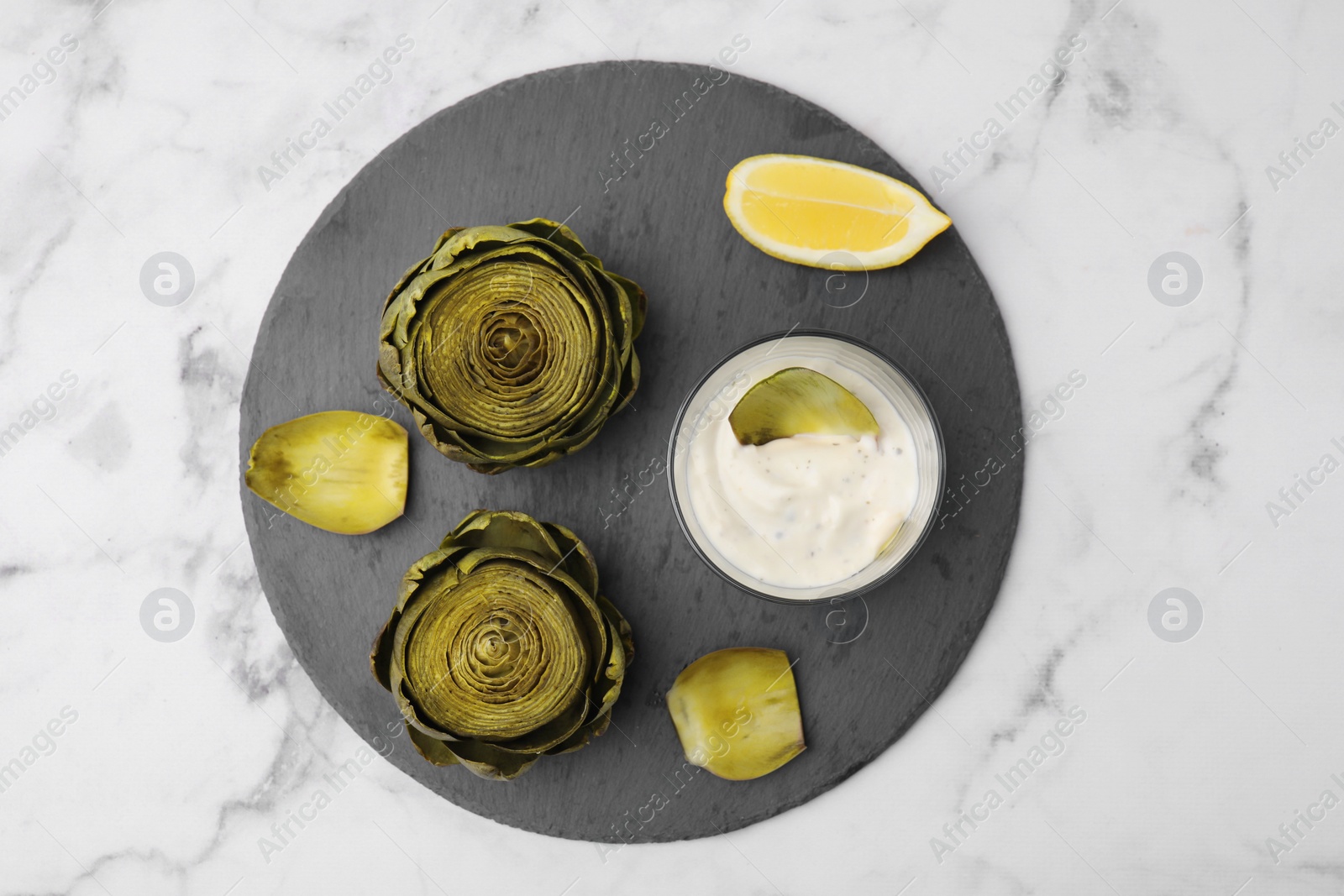 Photo of Delicious cooked artichokes with tasty sauce served on white marble table, top view