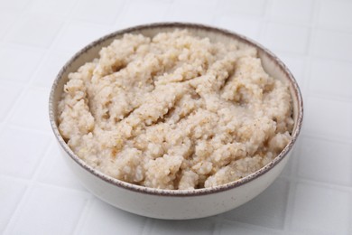 Delicious barley porridge in bowl on white table, closeup