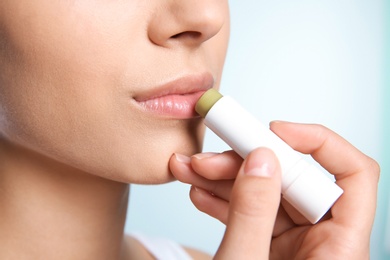 Young woman applying balm on her lips against color background, closeup