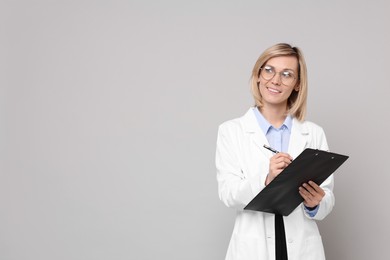 Photo of Smiling doctor with clipboard on grey background. Space for text