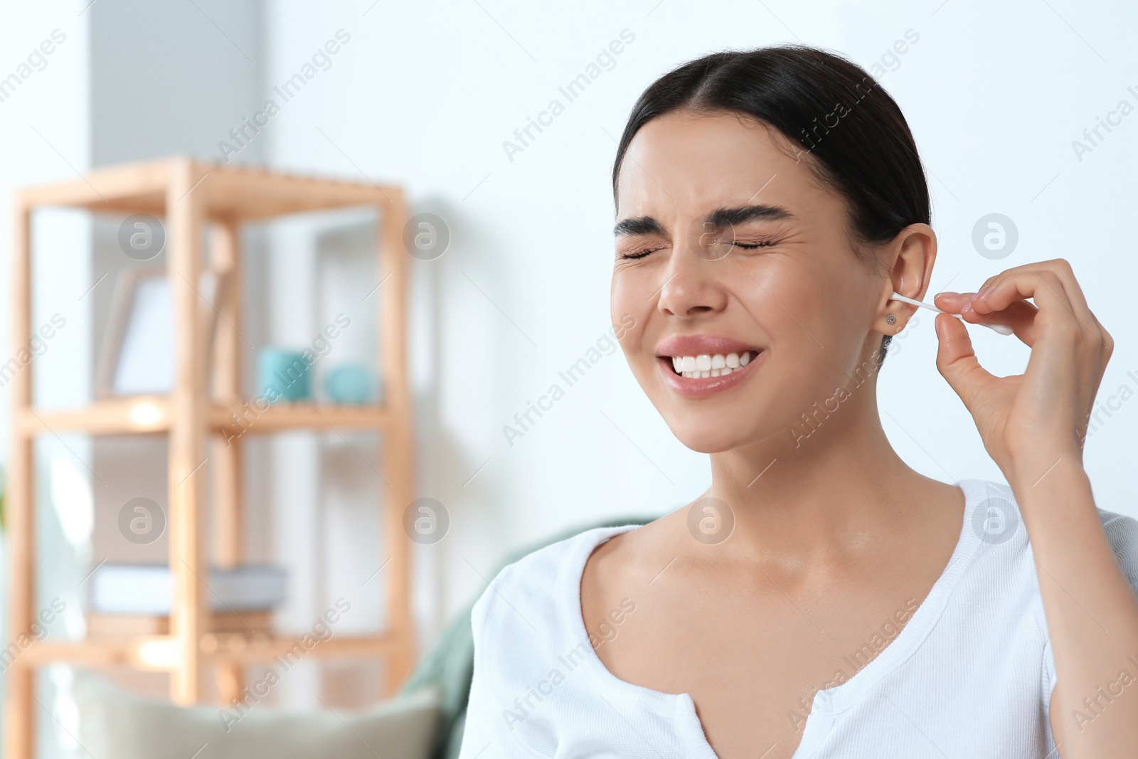 Photo of Young woman cleaning ear with cotton swab at home